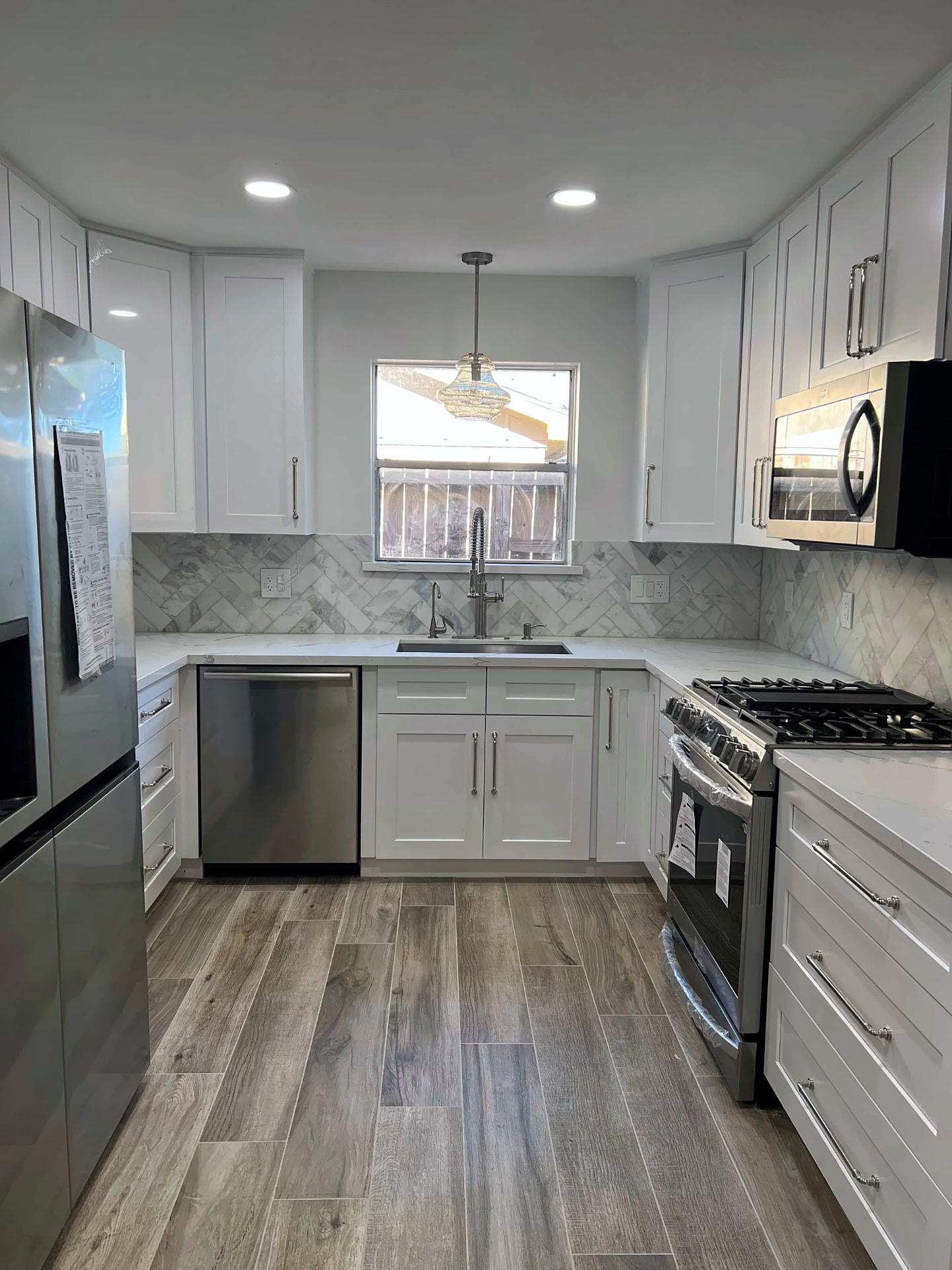 White shaker kitchen with a herringbone marble backsplash, stainless appliances, and wood-look tile flooring