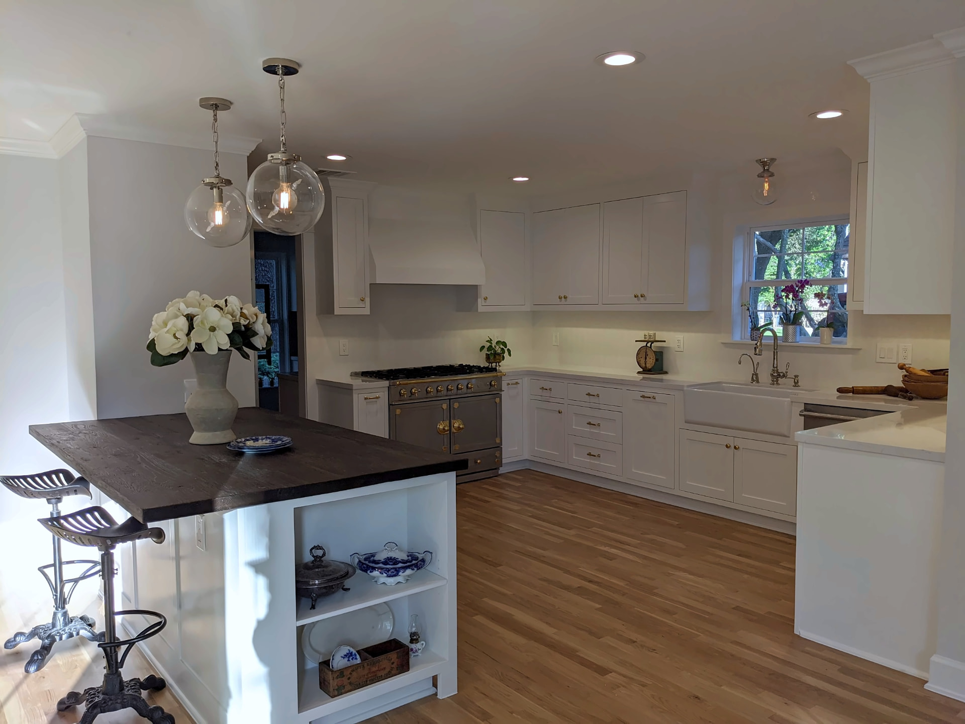 White kitchen remodel with a dark wood-top island, glass globe pendant lights, white range hood, and hardwood floors