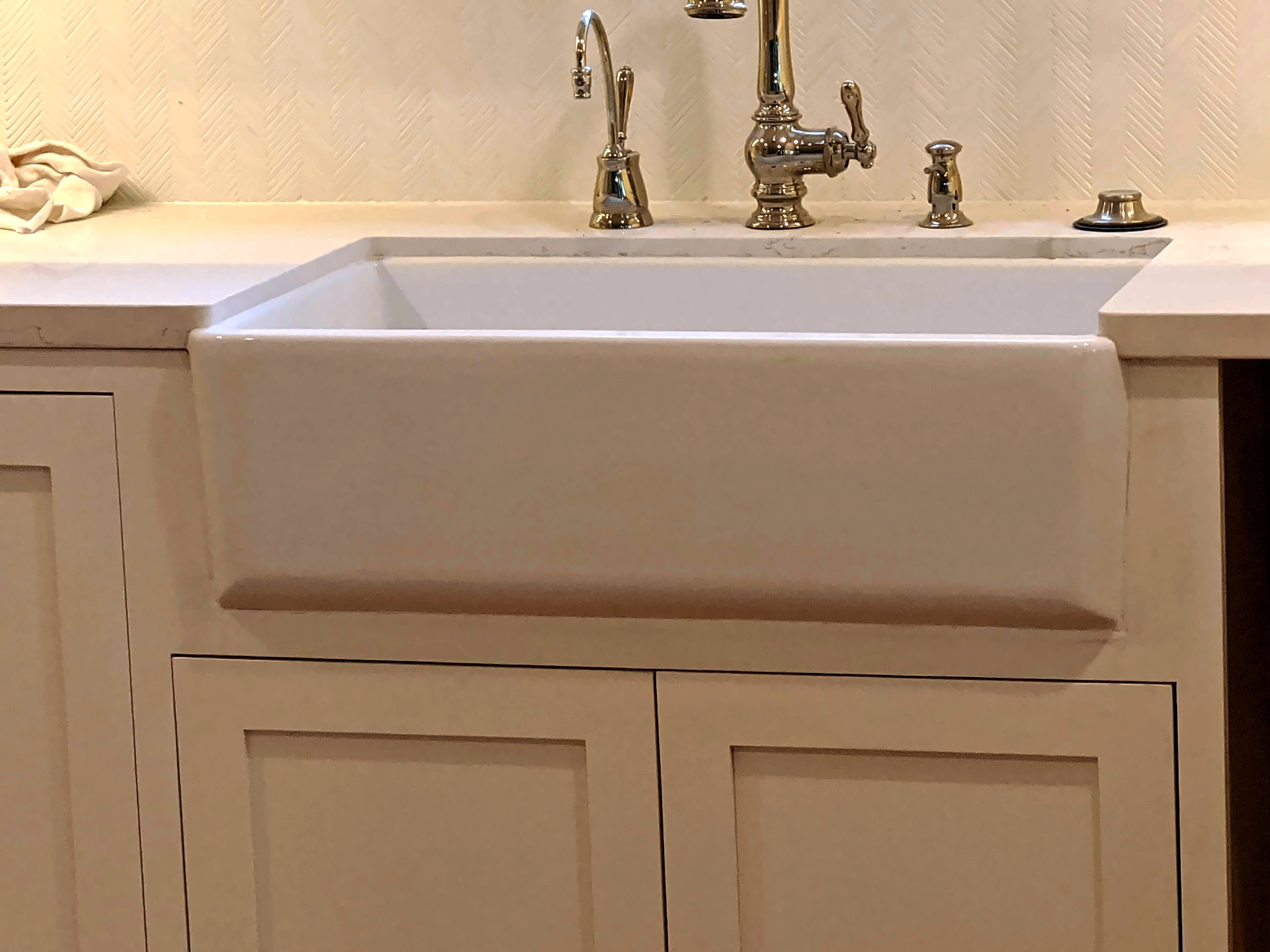 White apron-front farmhouse sink with a polished nickel bridge faucet against white cabinetry and a white countertop