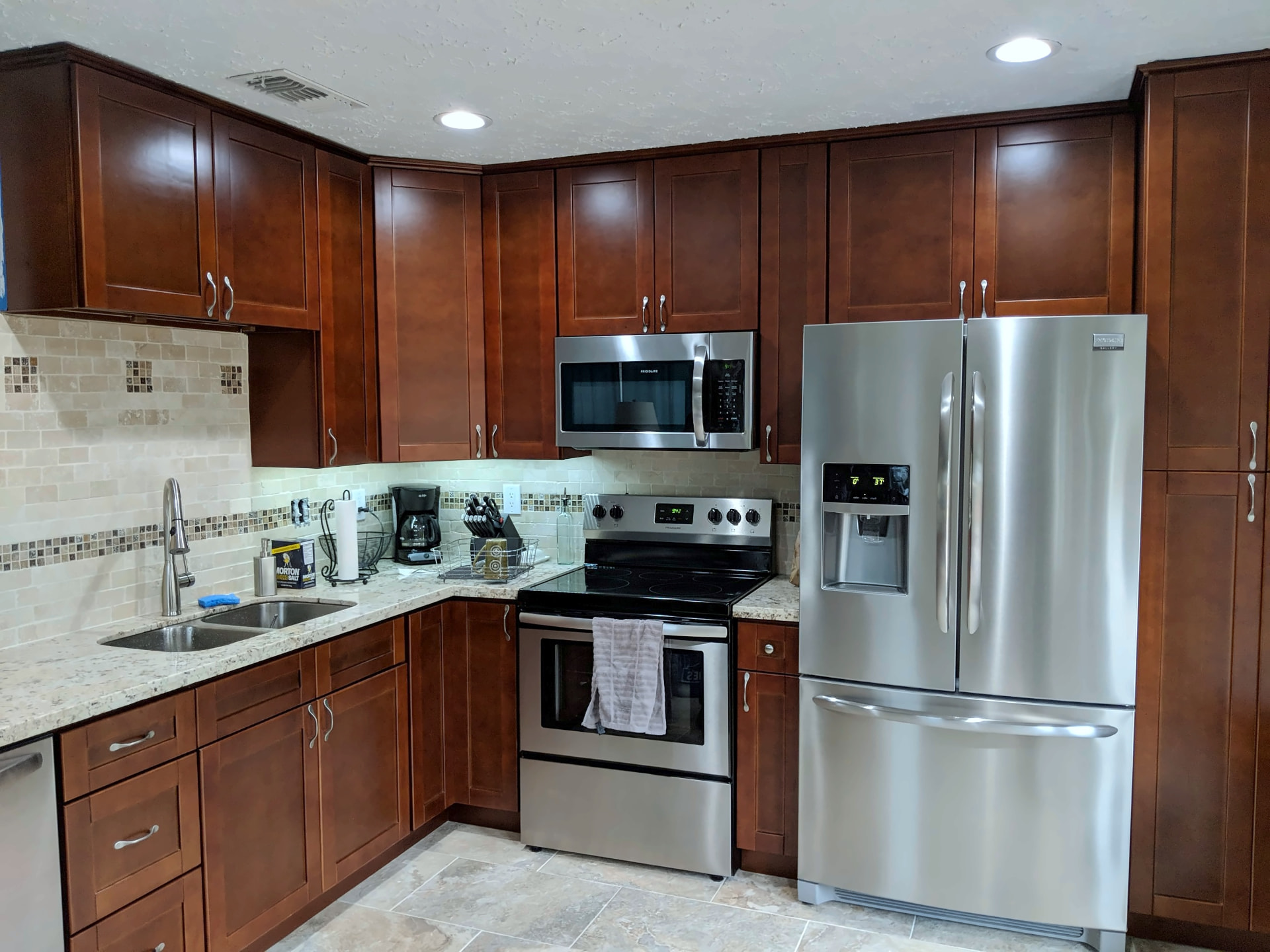 Cherry shaker kitchen with granite countertops, a stone tile backsplash, and stainless appliances