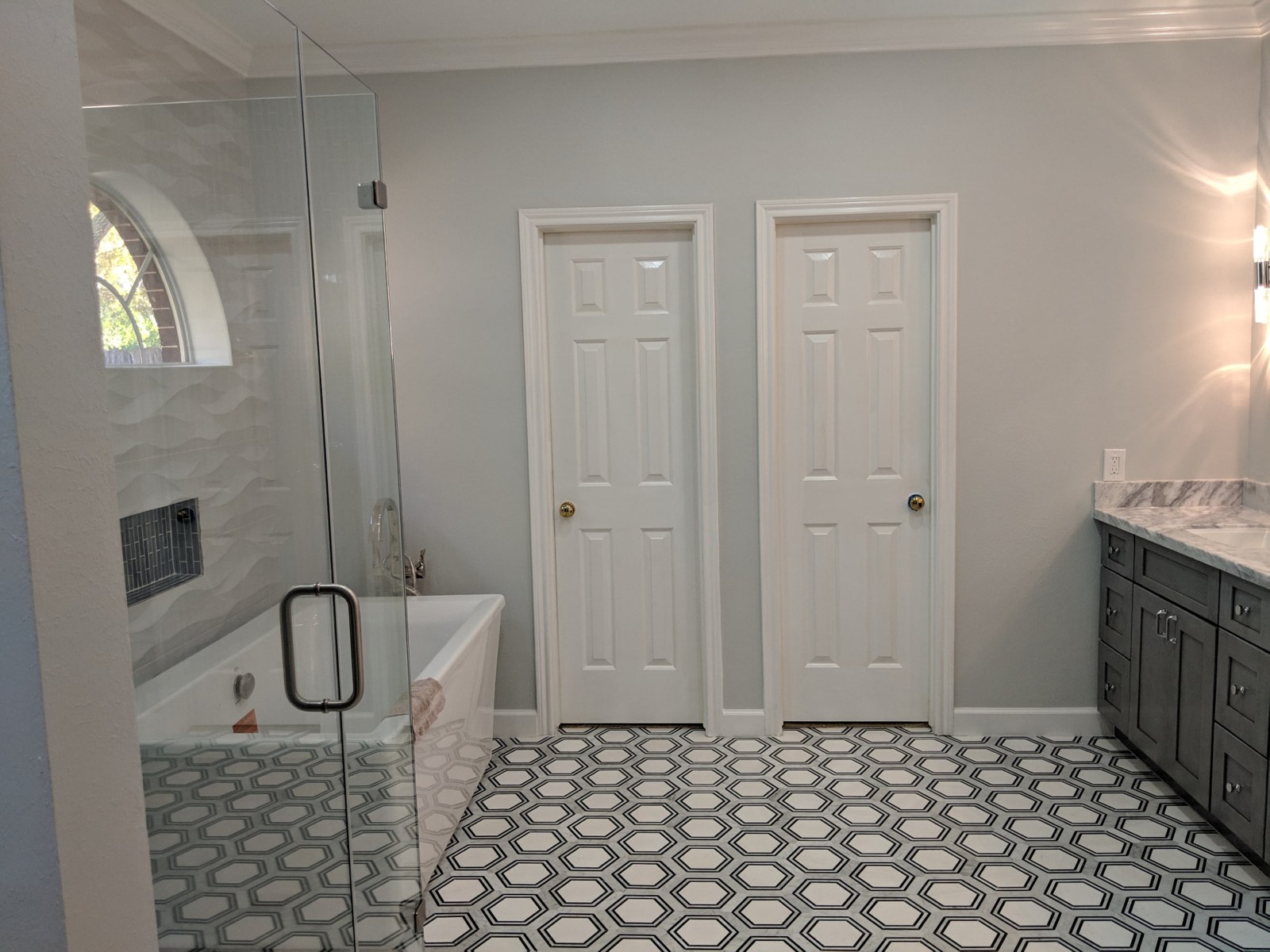 Finished bathroom with a dark double vanity, patterned floor tile, and frameless shower glass