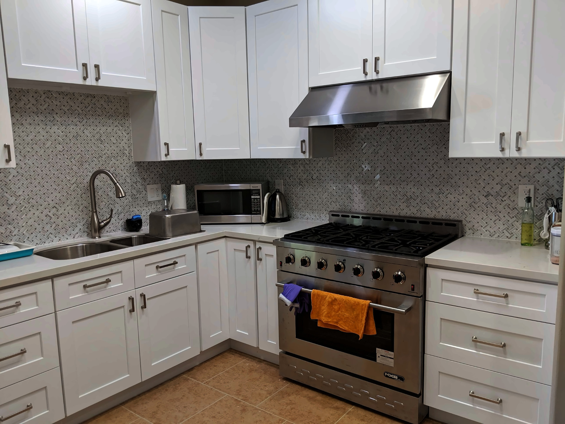 White shaker kitchen with a gray basketweave mosaic backsplash, professional gas range, and stainless hood