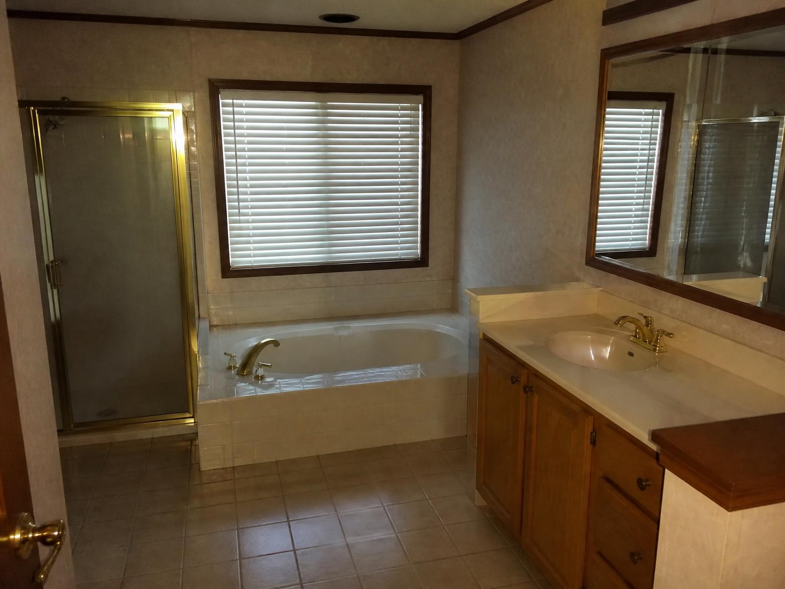 Before: Luxury primary bathroom with curbless walk-in shower, oak vanity, and freestanding tub